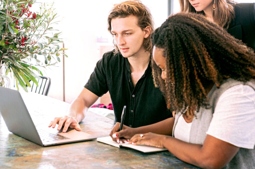 Three diverse colleagues collaborating around a laptop and notebook in a bright modern workspace